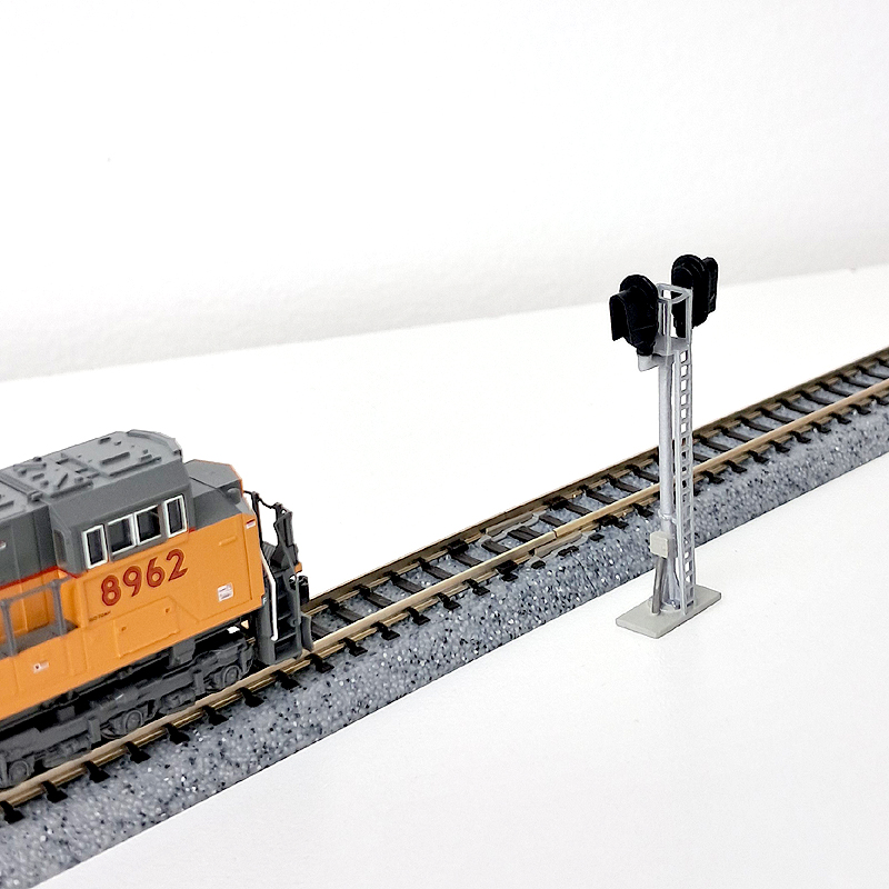 N scale bidirectional modern D-type signal next to train tracks.